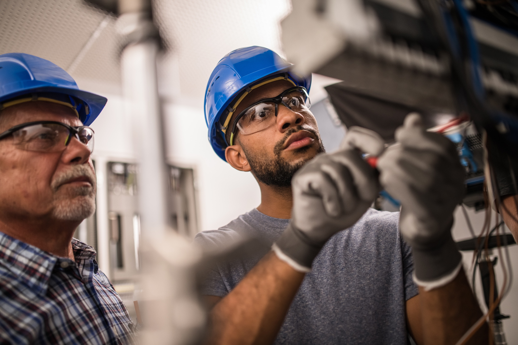 Photo of a senior caucasian and young African-American electrician working on a fuse box.